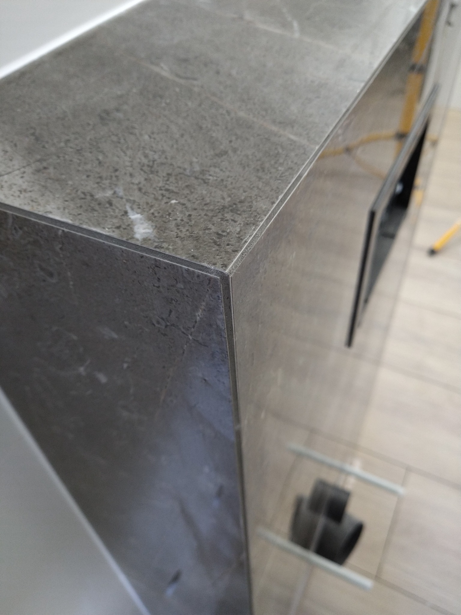 Szara, marmurkowa umywalka z szafką pod spodem, widoczne rury kanalizacyjne w tle. Minimalistyczny design.