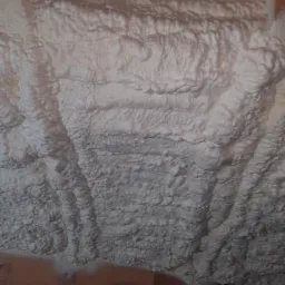 Pianka PUR o nierównej strukturze, zaaplikowana na poddaszu między krokwiami, widoczne drewniane elementy konstrukcji dachu.