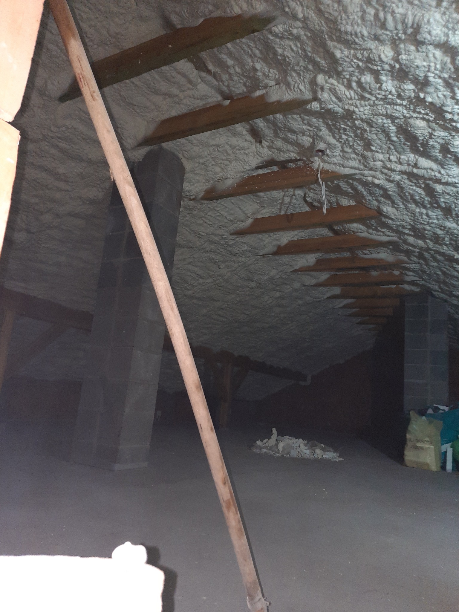 Poddasze po ociepleniu pianką poliuretanową, widoczne drewniane elementy konstrukcyjne i fragment komina, na podłodze resztki materiału izolacyjnego.
