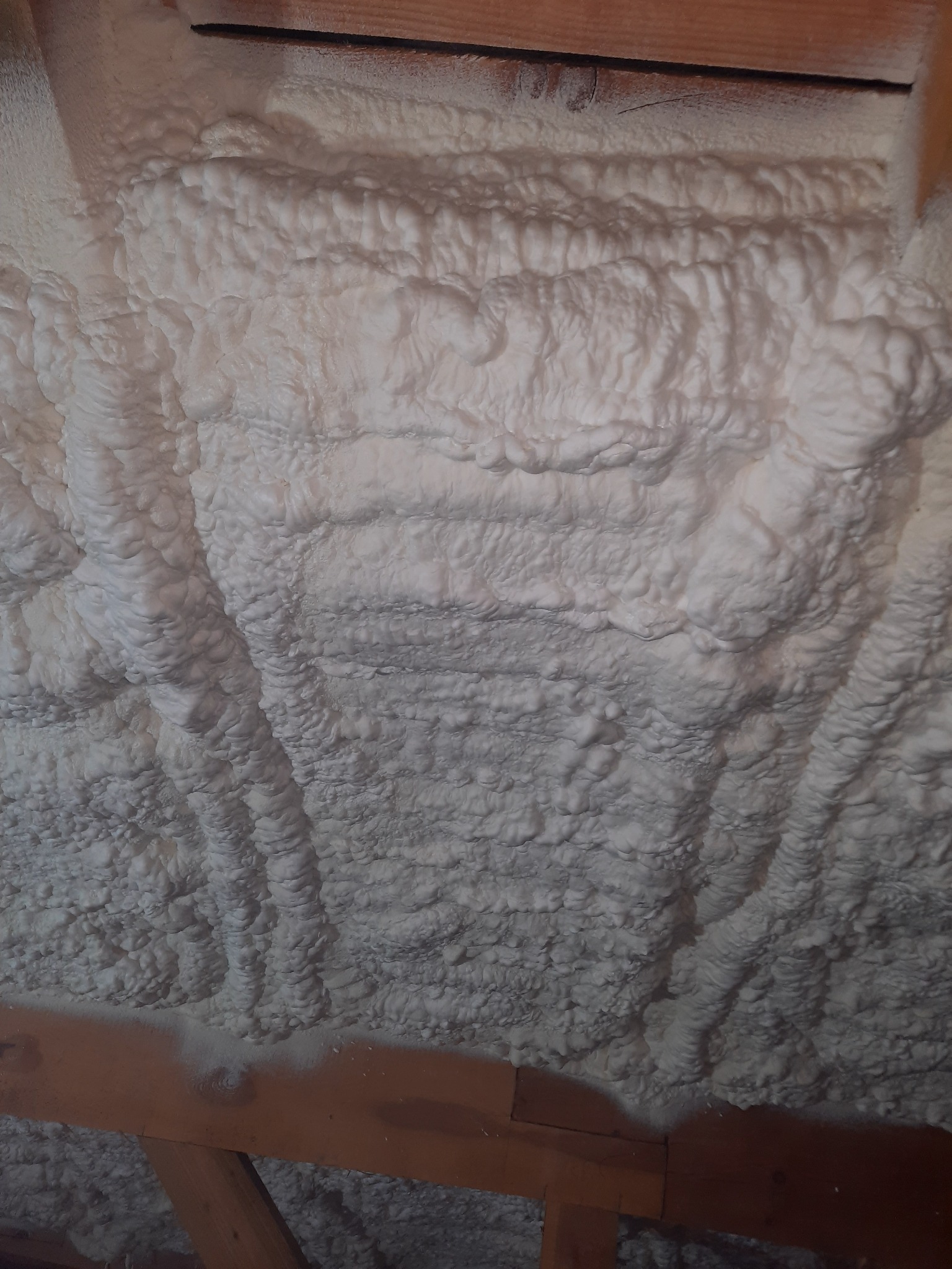 Pianka PUR o nierównej strukturze, zaaplikowana na poddaszu między krokwiami, widoczne drewniane elementy konstrukcji dachu.