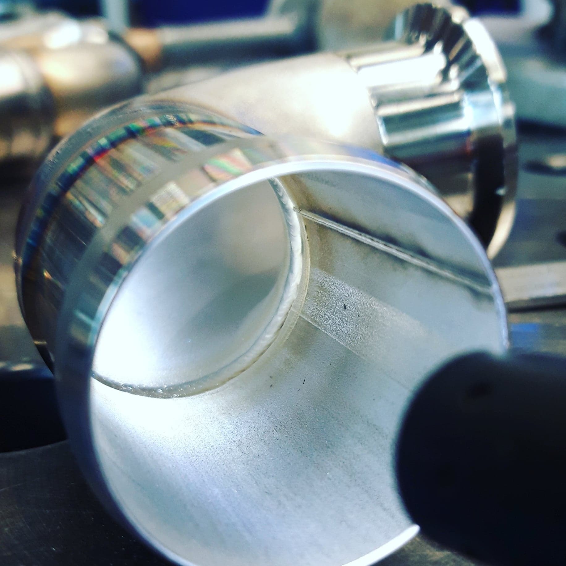 Szczegółowe ujęcie spawu na wewnętrznej stronie rury ze stali nierdzewnej, widoczne tęczowe zabarwienia na spoinie, z elementami konstrukcyjnymi w tle.