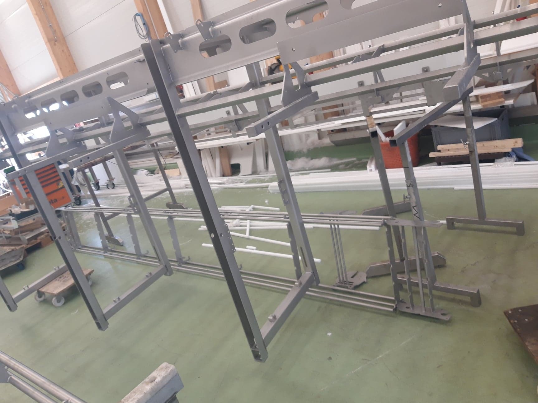 Konstrukcja metalowa, prawdopodobnie w trakcie malowania proszkowego, widoczne elementy do zawieszania detali, podłoga pokryta resztkami farby.