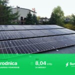 Instalacja paneli słonecznych na dachu domu jednorodzinnego, widok z góry pod lekkim kątem, z zielonym paskiem informacyjnym na dole prezentującym dane o produkcji energii.