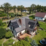 Dwuspadowy dom z panelami słonecznymi na dachu, widok z góry, otoczony zielenią.