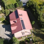 Widok z drona na dom z czerwoną dachówką i panelami fotowoltaicznymi zamontowanymi na połaci dachu.