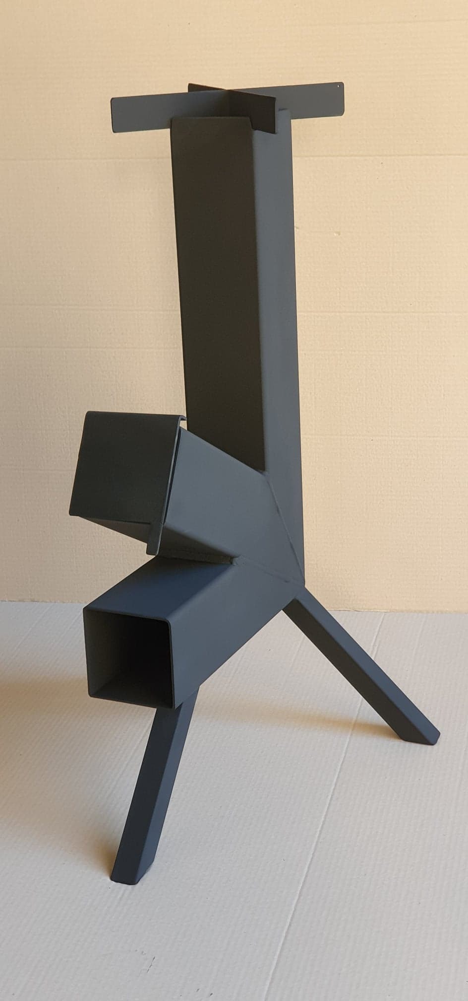 Metalowa konstrukcja pieca rakietowego pomalowana na szaro, widoczna na jasnym tle.