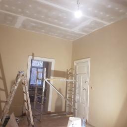 Przemysław Woźniak - Pokój w trakcie remontu: ściany w kolorze ecru, sufit z widocznymi łączeniami płyt karton-gips przed szpachlowaniem, drabina i rusztowanie w pomieszczeniu.