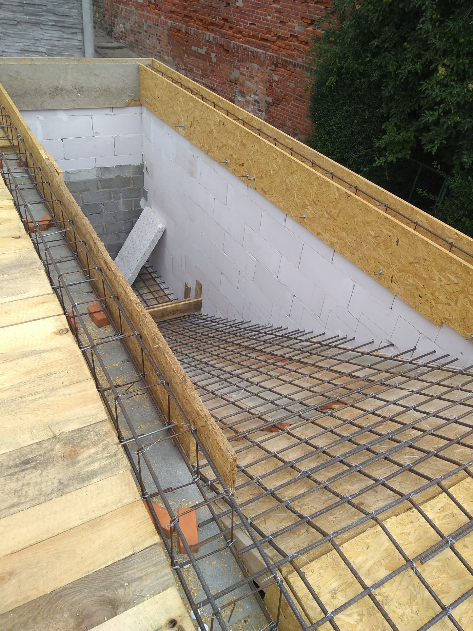 Zbrojenie stropu z siatki stalowej, drewniane szalunki i bloczki betonowe w trakcie budowy, widok z góry.