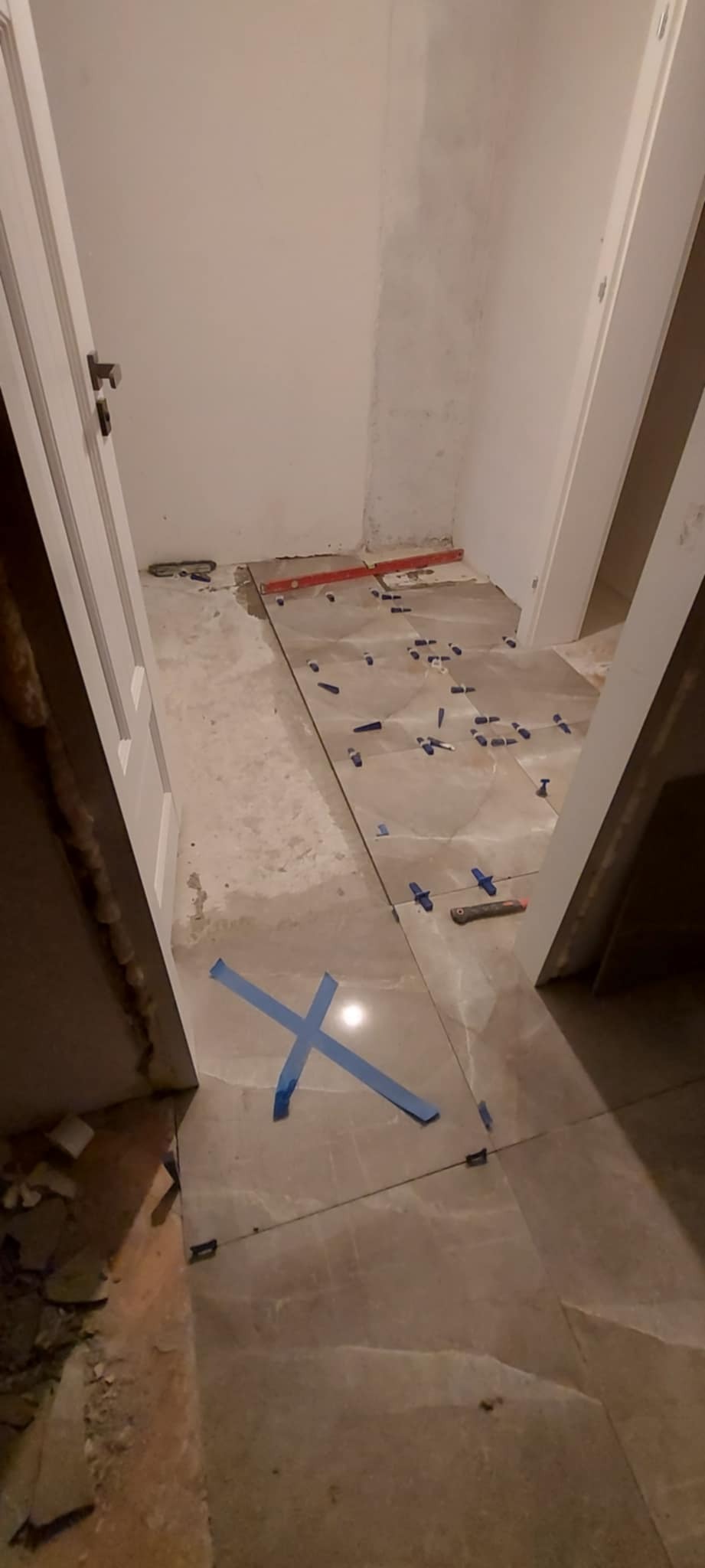 Ułożone płytki podłogowe w trakcie prac wykończeniowych, widoczne krzyżyki dystansowe, poziomica i nóż do cięcia płytek.