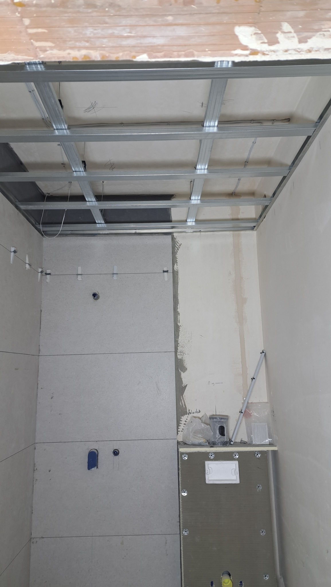 Montaż sufitu podwieszanego z metalowych profili i układanie płyt gipsowych na ścianach w trakcie prac remontowych w łazience.