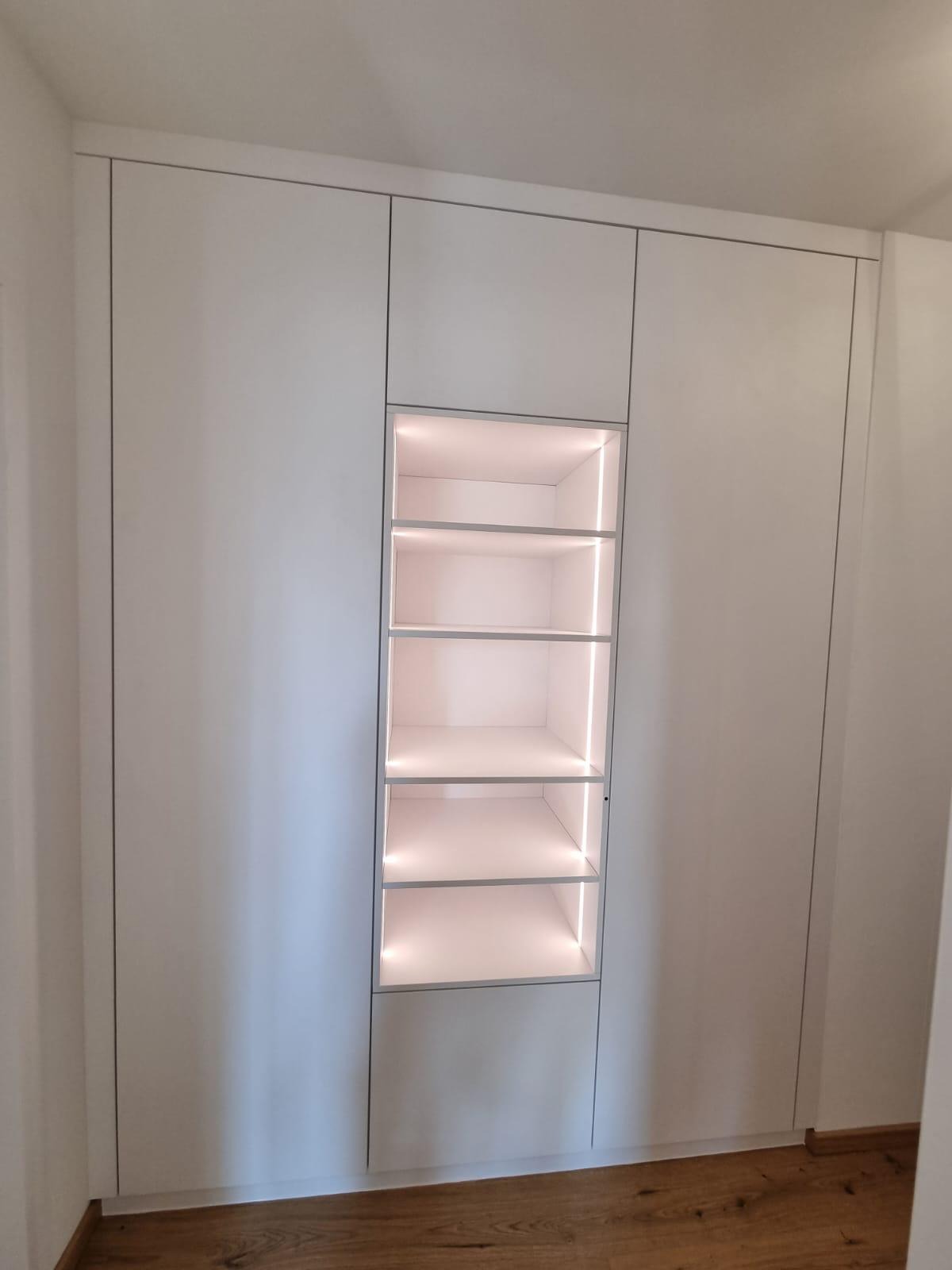 Biała szafa wnękowa z podświetlanymi półkami, widok na drewnianą podłogę