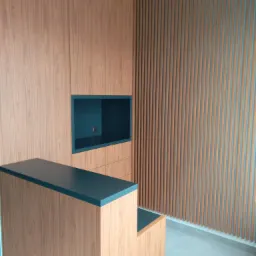 Drewniana zabudowa meblowa z półką i blatem w kolorze ciemnego turkusu, na tle ściany z pionowych listew w odcieniach brązu i turkusu, widok z dołu.