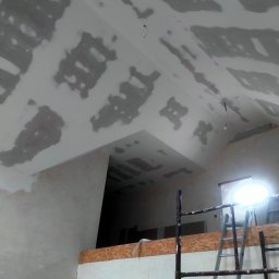 usługi remontowo wykończeniowe Paweł Paprocki - Skośny sufit po nałożeniu gładzi szpachlowej, widoczne ślady po łatach. Metalowe rusztowanie i drabina oparta o ścianę. W tle otwór w ścianie.