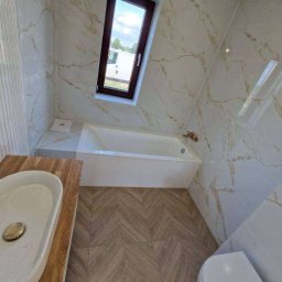 usługi remontowo wykończeniowe Paweł Paprocki - Nowoczesna łazienka z wanną, umywalką nablatową i oknem. Płytki imitujące marmur na ścianach, podłoga w jodełkę. Jasne, naturalne światło.