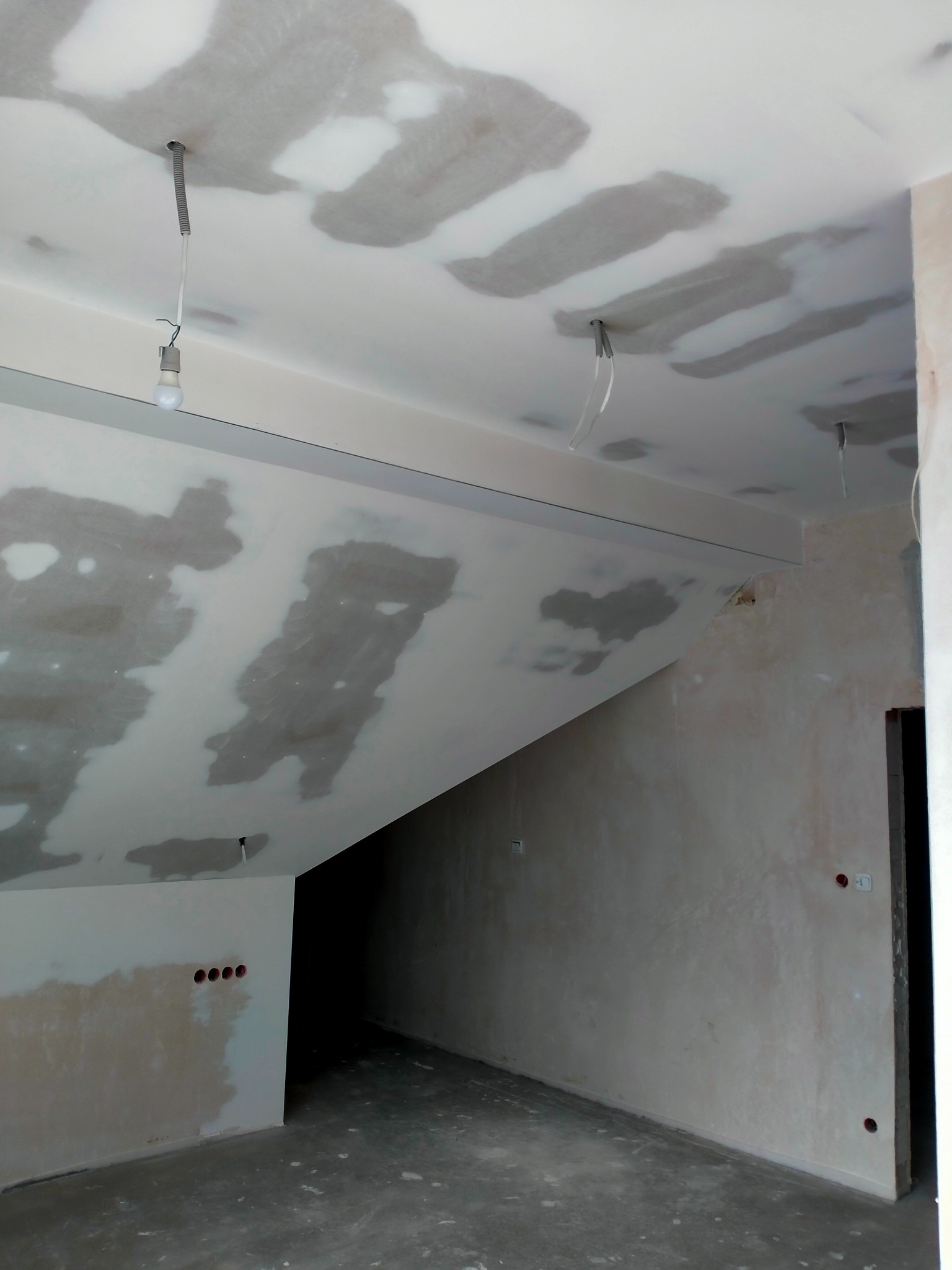 Poddasze w trakcie prac wykończeniowych: szpachlowane ściany i sufit z widocznymi przewodami elektrycznymi. Surowy stan przygotowany do dalszych prac.