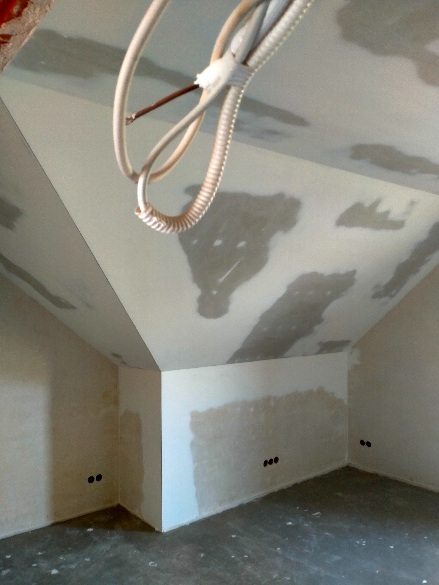 Poddasze w trakcie prac wykończeniowych: ściany i sufit częściowo pokryte gładzią, widoczne kable elektryczne. Stan surowy z elementami wykończenia.