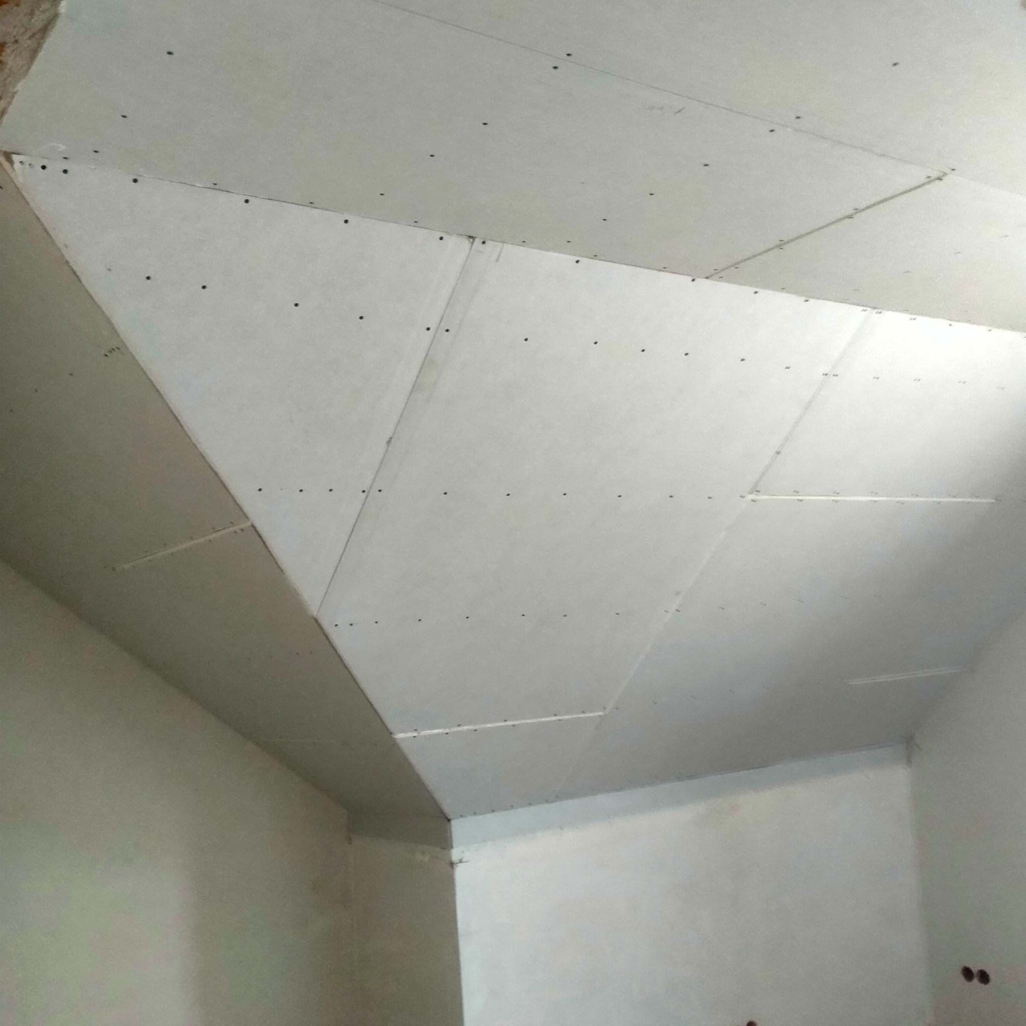 Skośny sufit z płyt kartonowo-gipsowych, mocowany na stelażu. Widoczne łączenia płyt i wkręty. Ściany w surowym stanie, przygotowane do dalszych prac wykończeniowych.