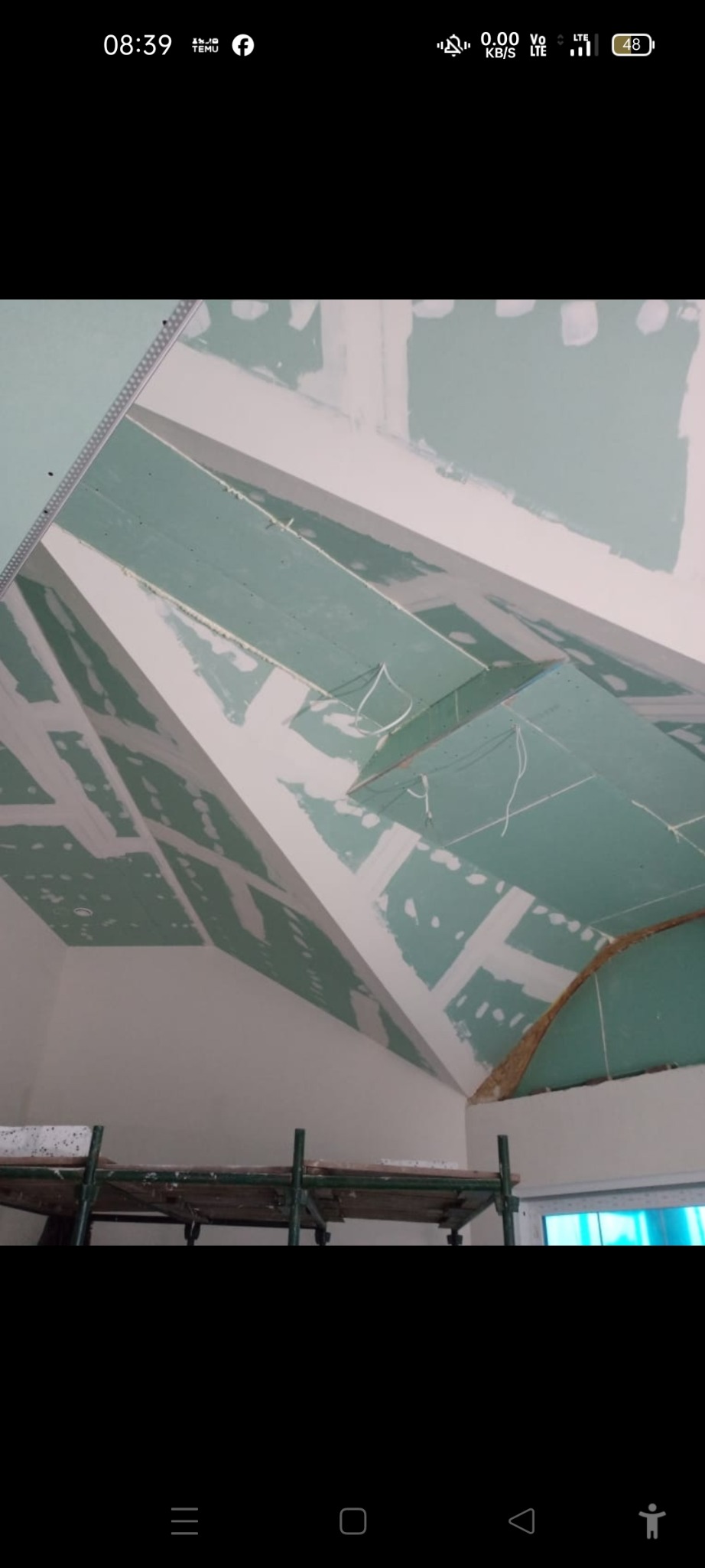 Skośny sufit z płyt karton-gips, częściowo wykończony gładzią, widoczne rusztowanie. Prace wykończeniowe w trakcie realizacji, oświetlenie naturalne.