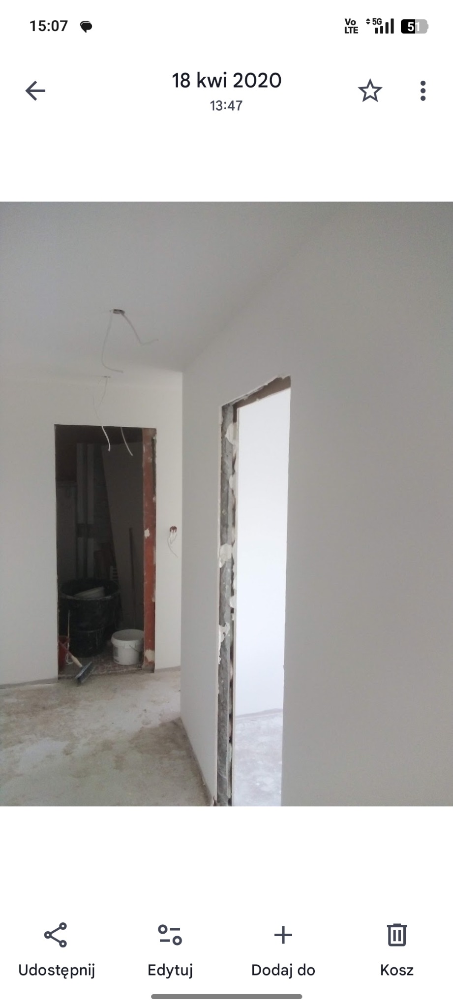 Wnętrze po gładziowaniu i malowaniu na biało, widoczne przygotowane otwory drzwiowe i kable oświetleniowe. Podłoga surowa, w tle wiadro i narzędzia.