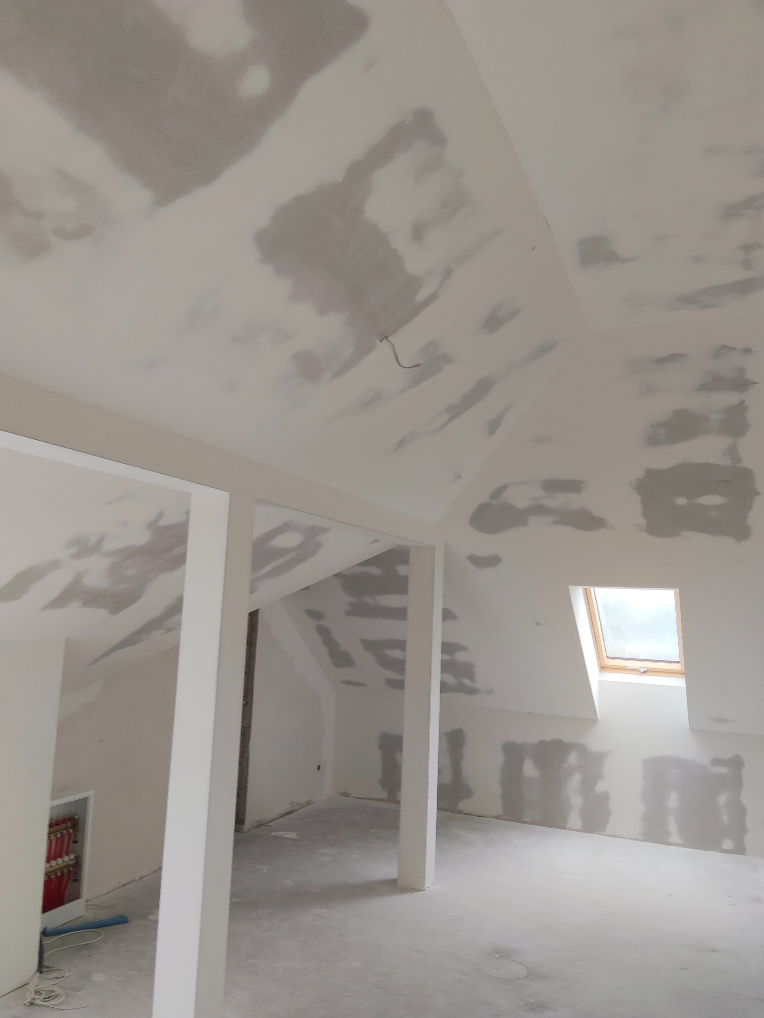 Poddasze po szpachlowaniu, widoczne ślady po łatach na skosach i suficie, okno dachowe. Przygotowanie do malowania ścian i sufitu.