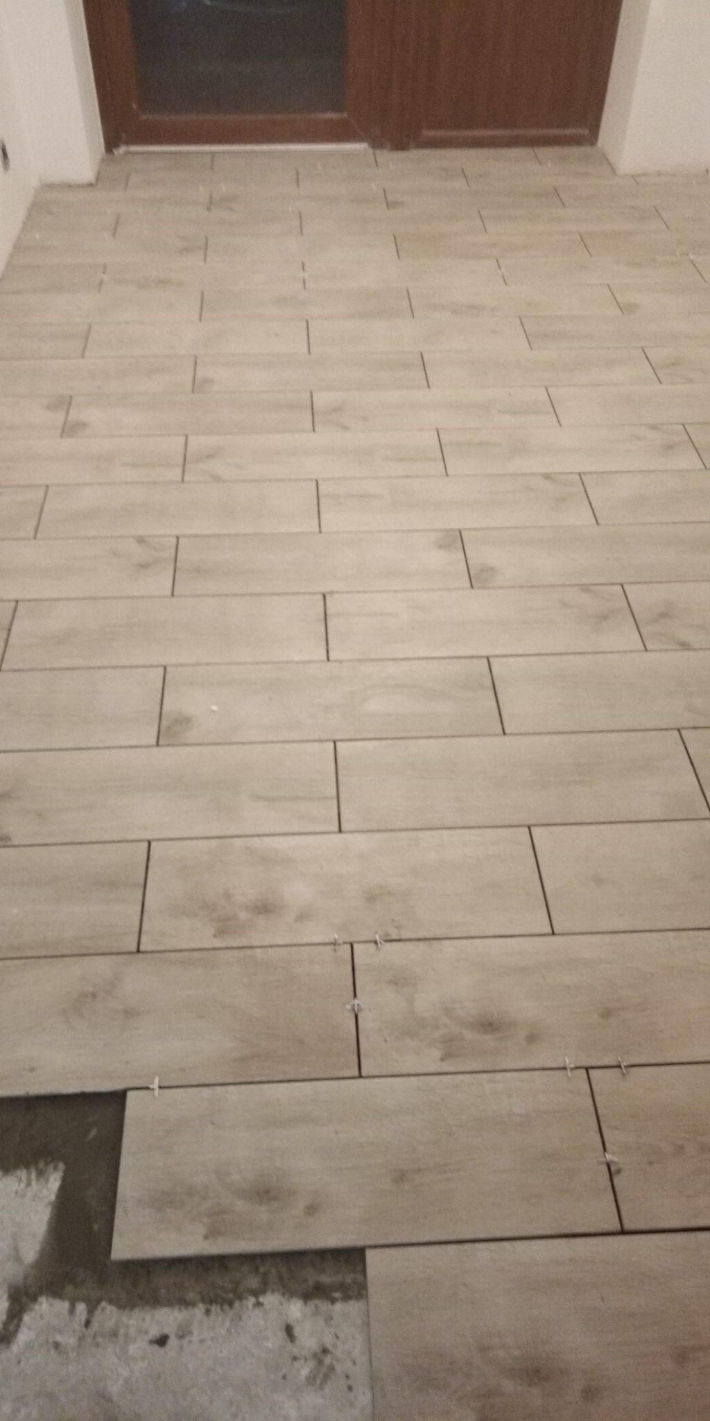 Układanie podłogi z płytek imitujących drewno, widoczne krzyżyki dystansowe i fragment nieukończonej powierzchni.