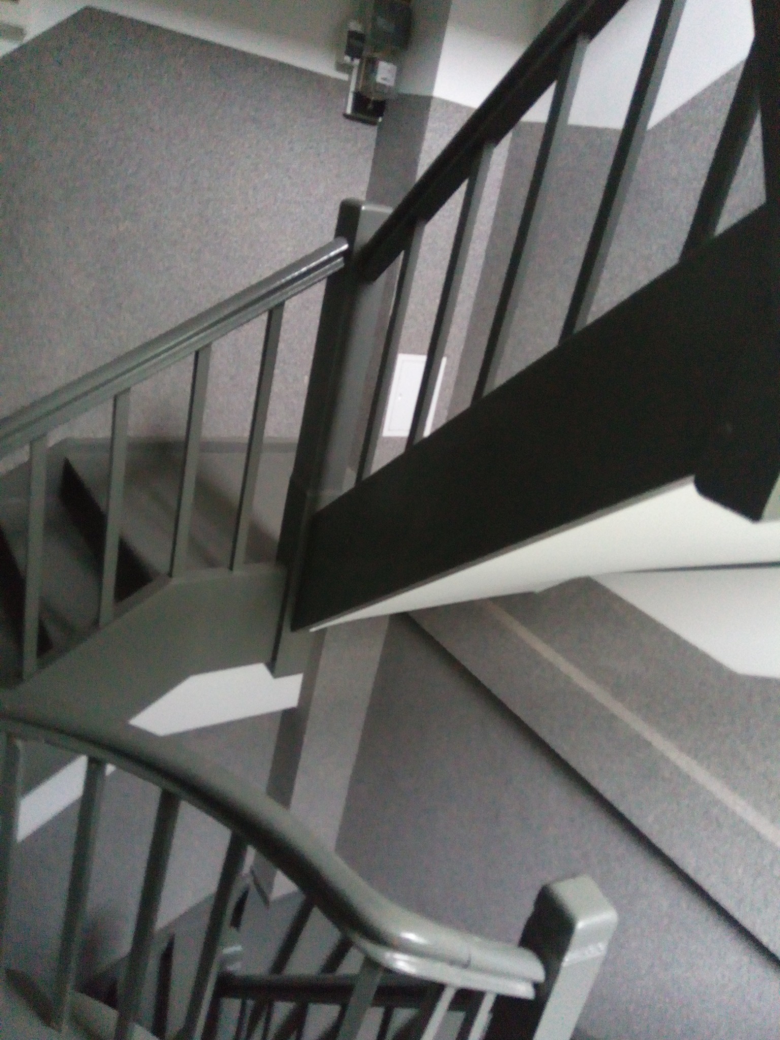 Widok z góry na schody z szarą wykładziną i pomalowanymi na szaro poręczami.