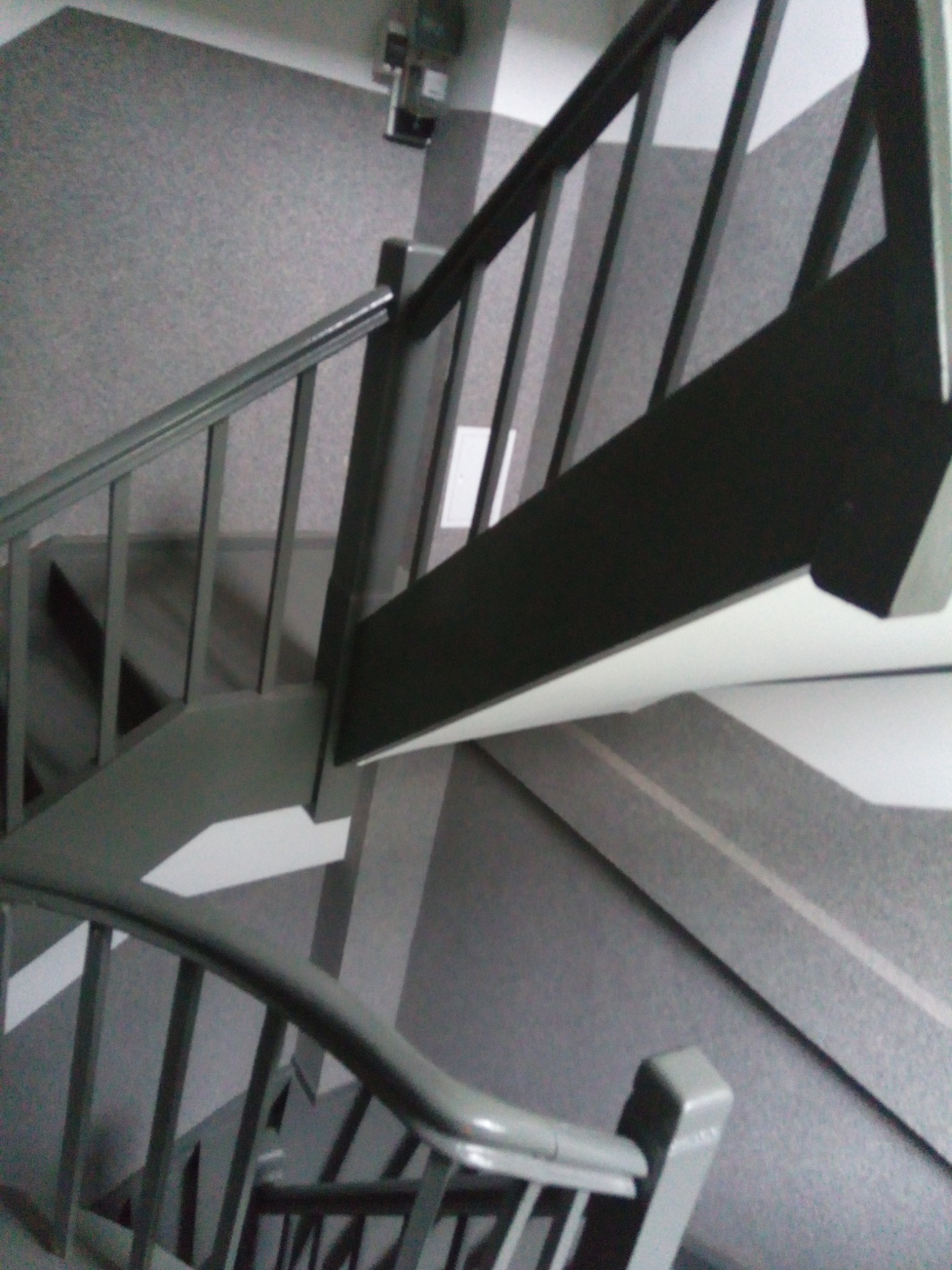 Klatka schodowa z szarymi ścianami i pomalowanymi na szaro schodami oraz barierkami, widok z góry.