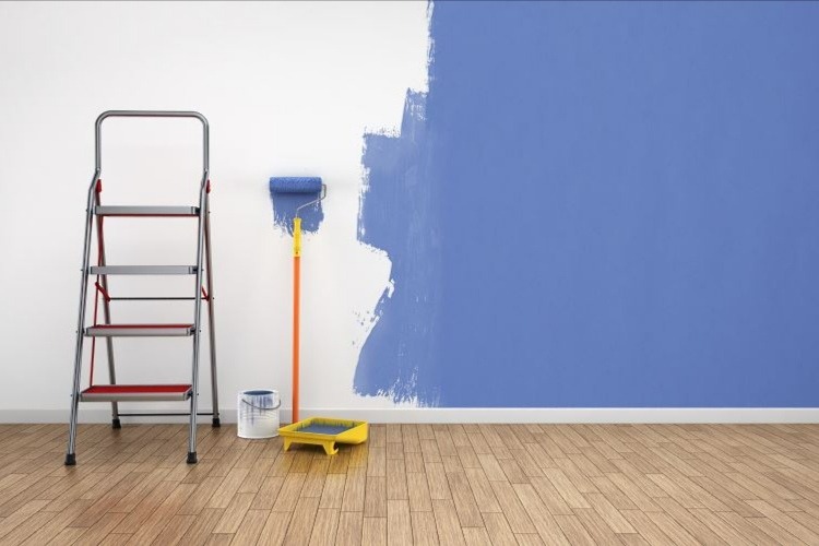 Świeżo pomalowana na niebiesko ściana z widocznymi śladami wałka, drabina, wałek do malowania, kuweta i wiaderko z farbą na drewnianej podłodze.