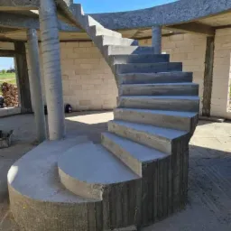 Wewnętrzne spiralne schody w surowym stanie, wykonane z betonu, w trakcie budowy domu z białej cegły.