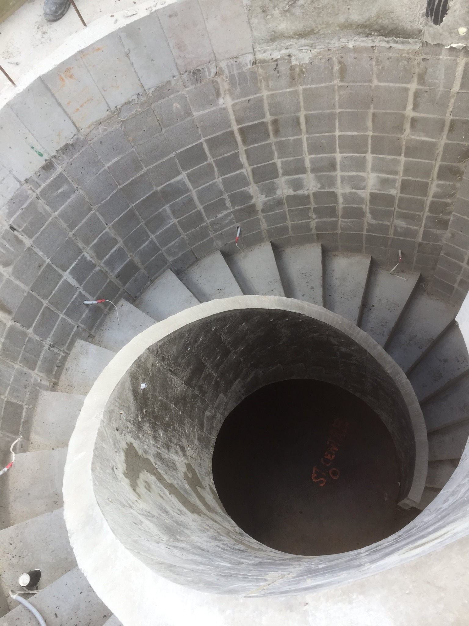 Wnętrze betonowej klatki schodowej spiralnej w trakcie budowy, widok z góry, widoczne zbrojenia i szalunki, na dole napis ST CENTRUM.