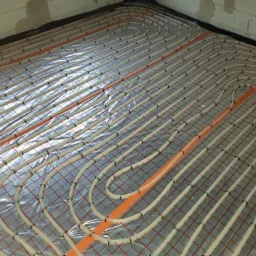 Rozłożone rury ogrzewania podłogowego na folii izolacyjnej z siatką, widoczne fragmenty ścian z betonu komórkowego.