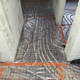 Instalacja ogrzewania podłogowego w surowym stanie, rury grzewcze ułożone na folii z siatką, widoczne bloczki z betonu komórkowego.