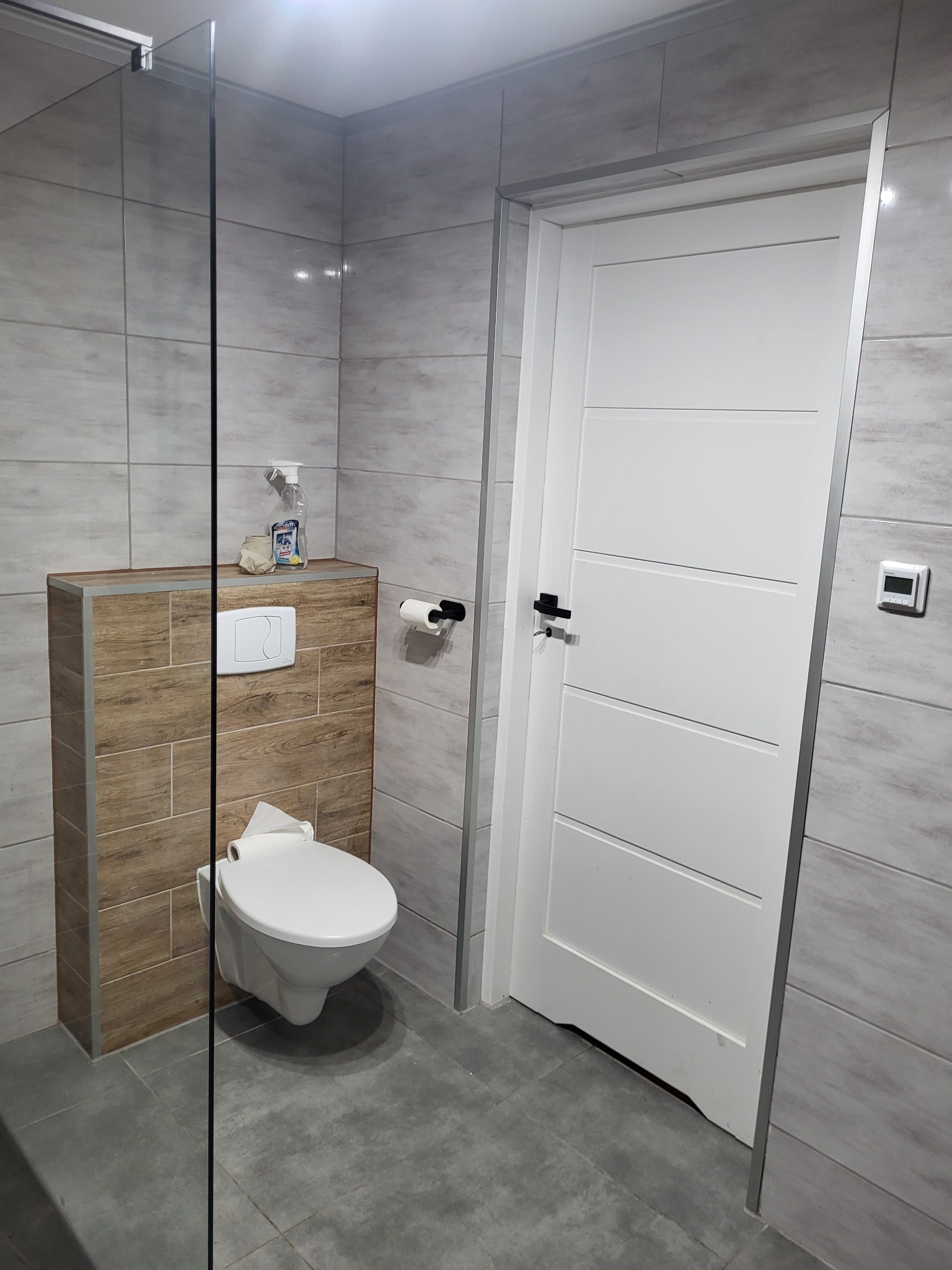 Nowoczesna łazienka z podwieszaną toaletą, szarymi płytkami imitującymi kamień i białą, panelową ścianą działową.