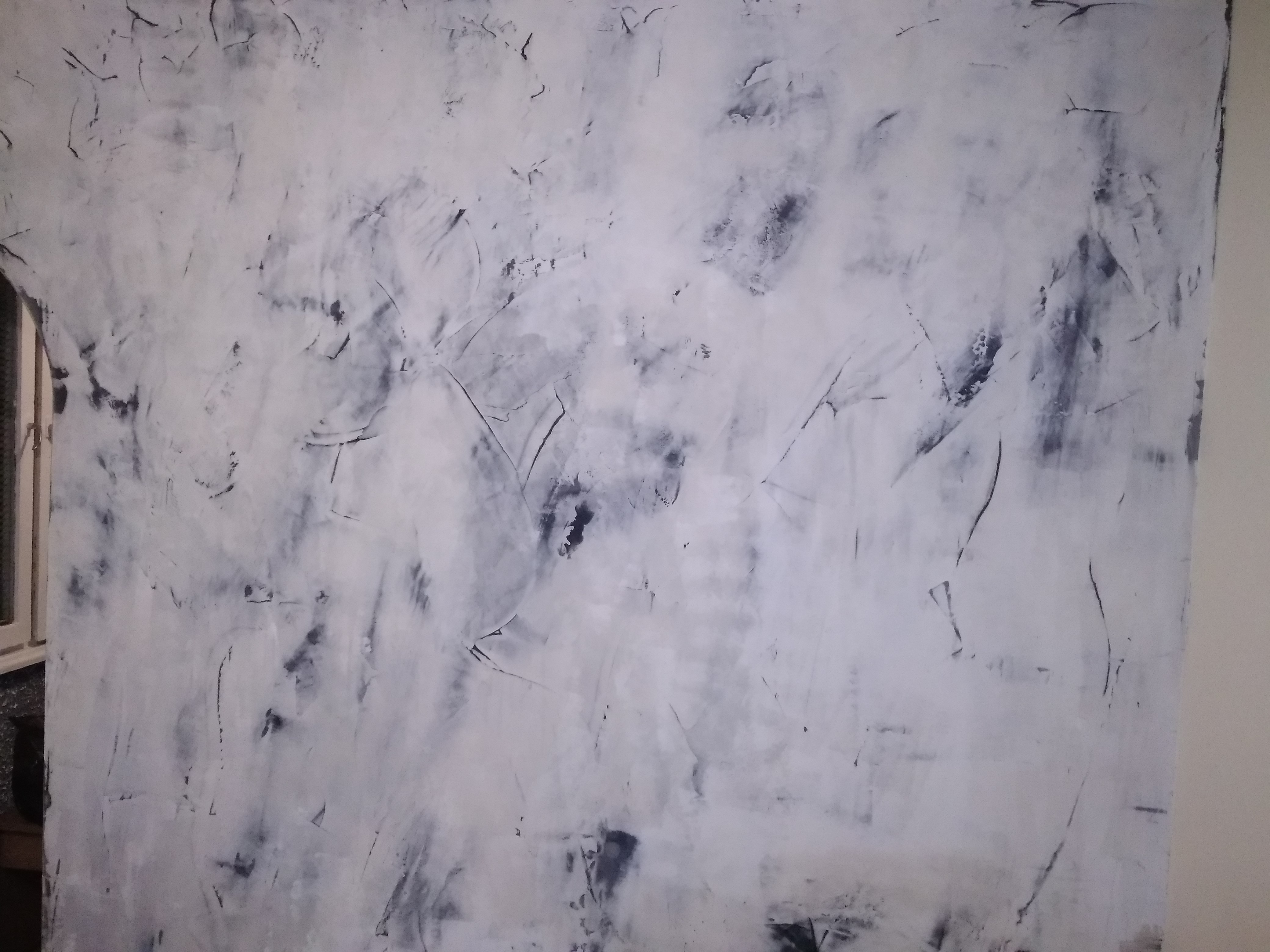 Ściana pokryta białą farbą z widocznymi śladami pędzla i ciemnymi smugami, imitująca efekt dekoracyjny, z fragmentem okna po lewej stronie.