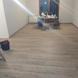 Edmar - Ułożone panele podłogowe w pokoju z widocznym stołem roboczym, wiadrem i drabiną malarską w tle.