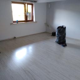 Edmar - Pusty pokój w Żywcu po remoncie, z nową podłogą z paneli, widoczny worek na śmieci i elementy instalacji elektrycznej przy podłodze.