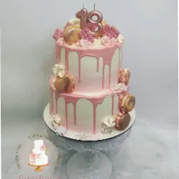 Dwupiętrowy tort urodzinowy z różowym lukrem, makaronikami i czekoladkami, udekorowany świeczkami w kształcie liczby 18, umieszczony na białym, ażurowym stojaku.