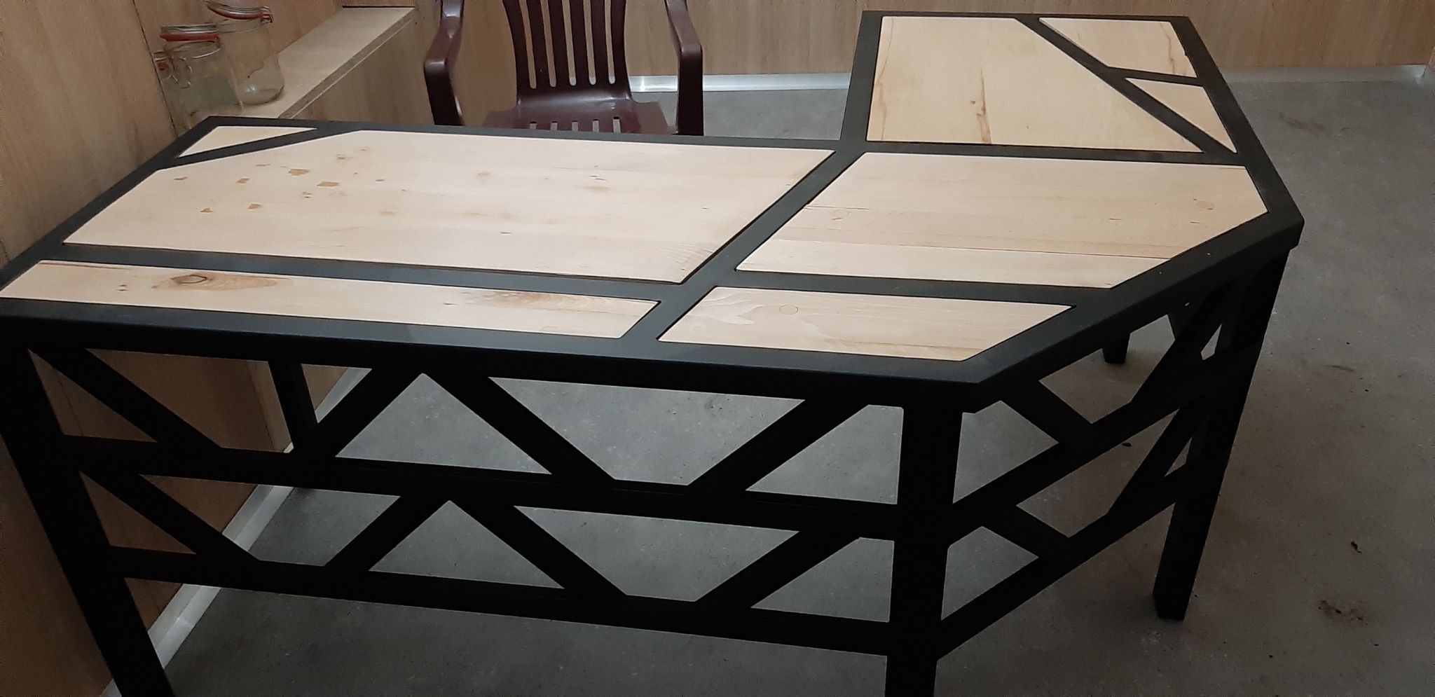 Narożne biurko z jasnego drewna z czarną metalową konstrukcją, widoczne geometryczne wzory na podstawie.