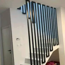 Nowoczesne schody z białą konstrukcją i czarną, minimalistyczną balustradą pionową, widoczne z dołu, z fragmentem sofy w kadrze.