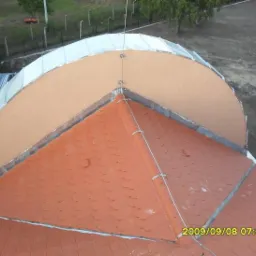 Widok z góry na fragment dachu z czerwoną dachówką karpiówką i dobudowaną, ocieploną półokrągłą konstrukcją z blachy i tynku.