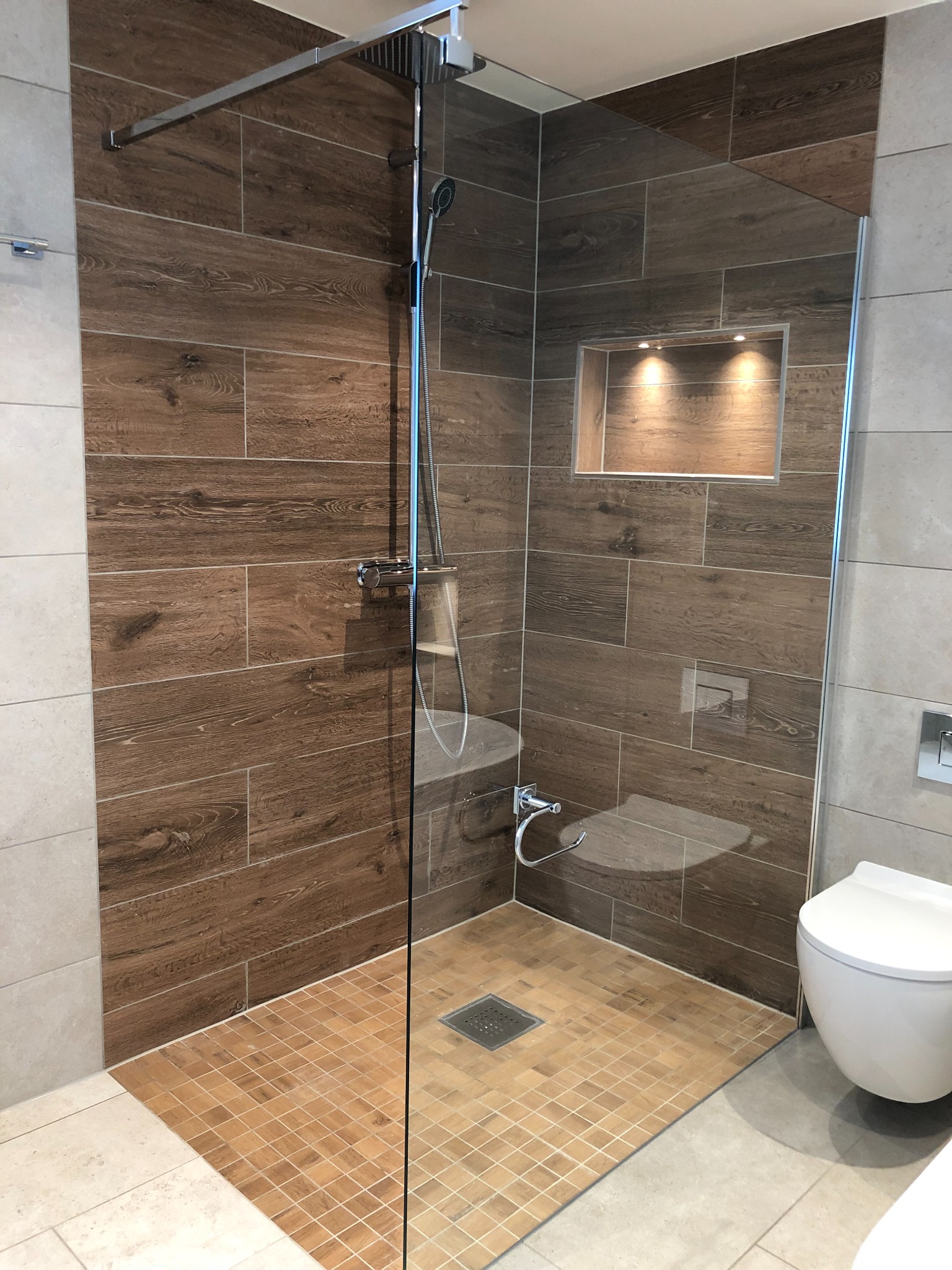 Nowoczesna kabina prysznicowa walk-in z drewnopodobnymi płytkami i wnęką z oświetleniem w Ljungskile. Uwagę zwraca odpływ liniowy w podłodze i minimalistyczna armatura.