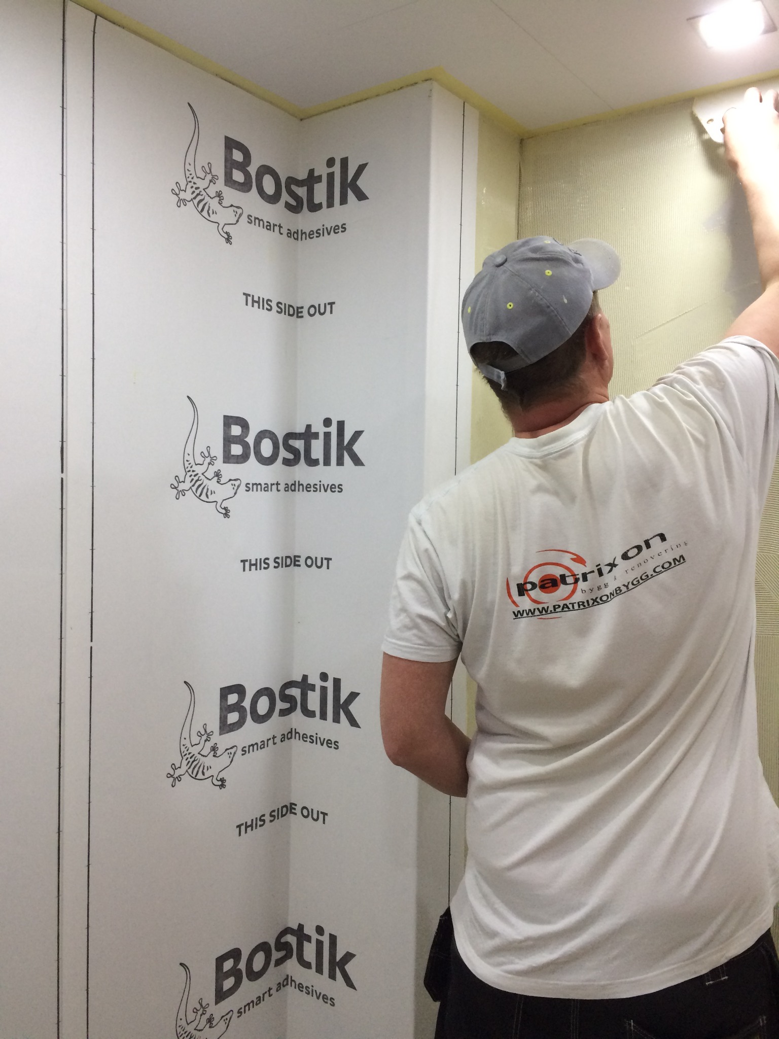 Pracownik w koszulce z logo firmy Patrixon nakłada gładź na ścianę wykończoną płytami izolacyjnymi z nadrukowanym logo Bostik