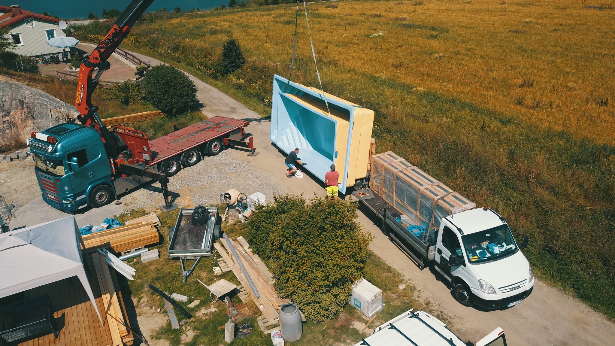 Montaż prefabrykowanej modułowej konstrukcji, prawdopodobnie basenu, za pomocą dźwigu na działce, widok z góry.
