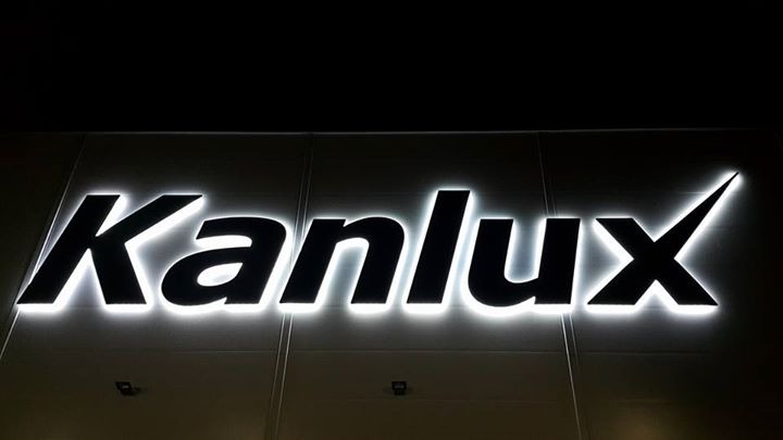 Podświetlany szyld z nazwą 'Kanlux' na elewacji budynku, wykonany z czarnych liter z białym podświetleniem krawędziowym.
