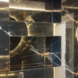 Czarne marmurowe płytki z złotymi żyłami tworzą półki we wnęce, podświetlone od góry, z czarnym włącznikiem światła na ścianie i fragmentem armatury.