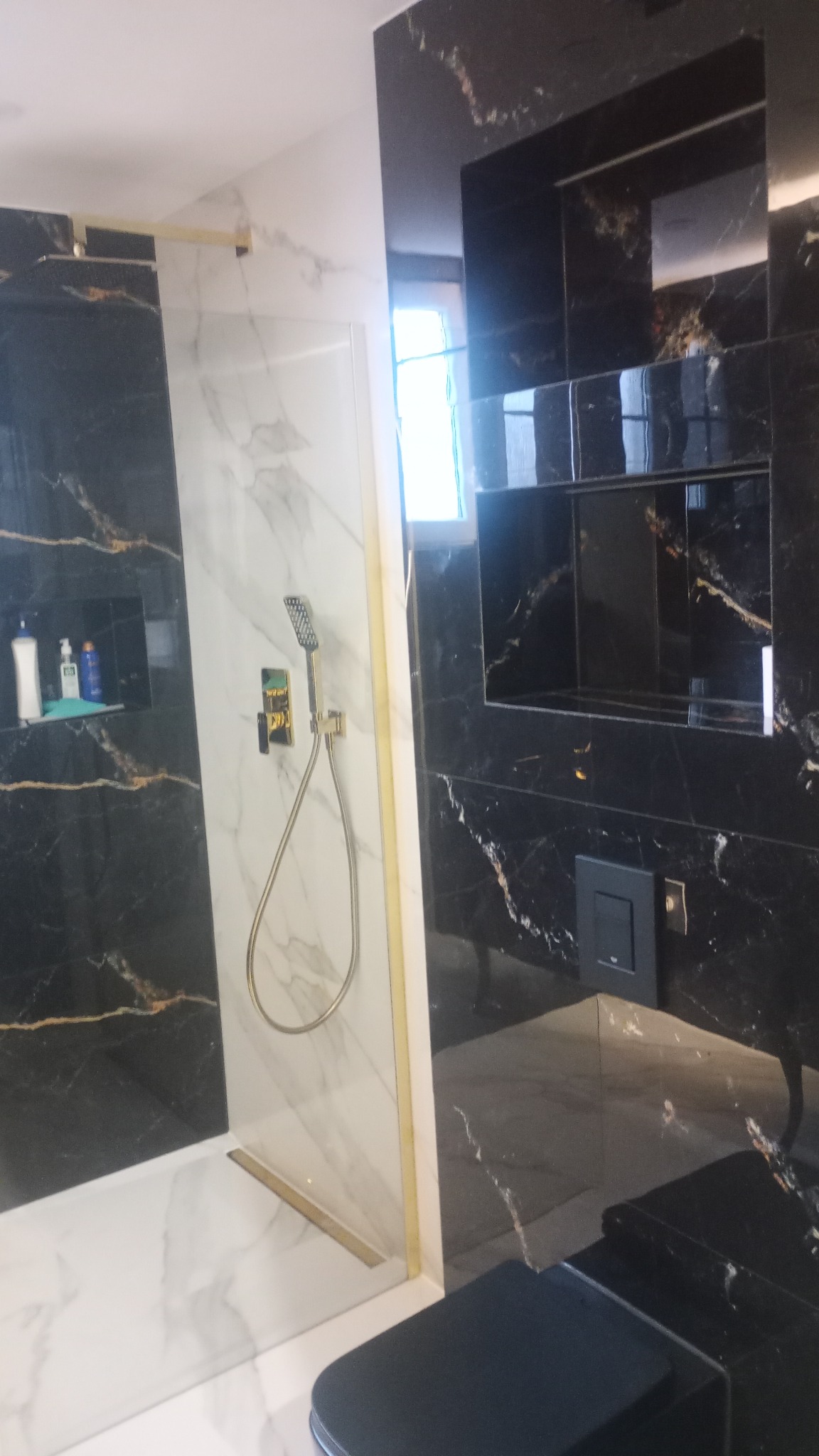 Kabina prysznicowa walk-in z czarnymi marmurkowymi płytkami i złotymi akcentami w łazience w Łętowni, widoczne półki w ścianie i deszczownica.