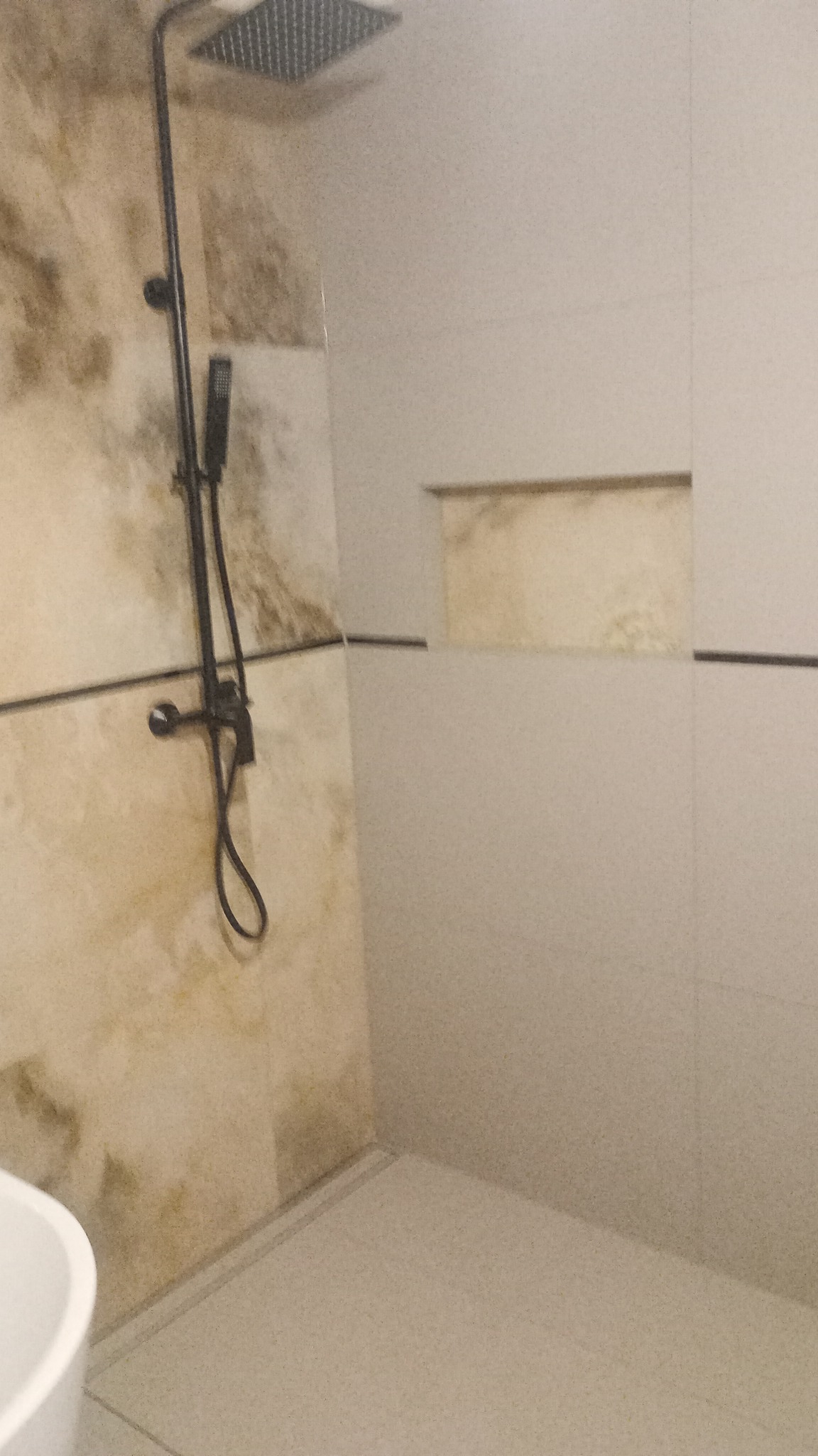 Nowoczesna kabina prysznicowa z deszczownicą w kolorze czarnym, beżowe płytki imitujące kamień na jednej ścianie, jasnoszare płytki na pozostałych ścianach i podłodze, wnęka w ścianie wykończona...