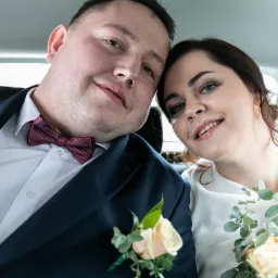 Uśmiechnięta para młoda w samochodzie, zbliżenie na twarze, bukiet kwiatów i bordowa mucha.