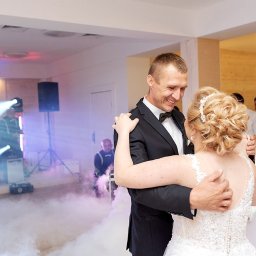 DS. PRO STUDIO - Para młoda w pierwszym tańcu, otoczona sztuczną mgłą, w tle DJ i goście, oświetlenie sceniczne.