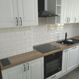 MEBLE-Koźlak Paweł - Nowoczesna biała kuchnia z drewnianym blatem, czarnymi uchwytami i płytkami w stylu metra, z czarnym okapem i płytą indukcyjną.